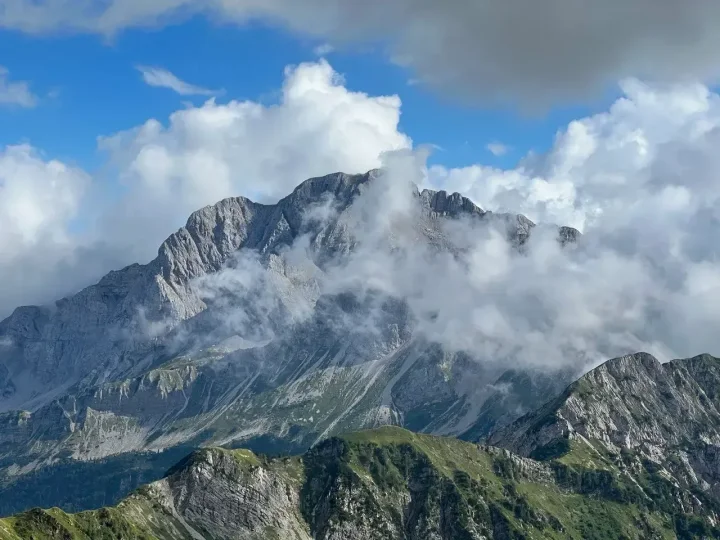 Cima rocciosa tra le nuvole sopra pendii verdi